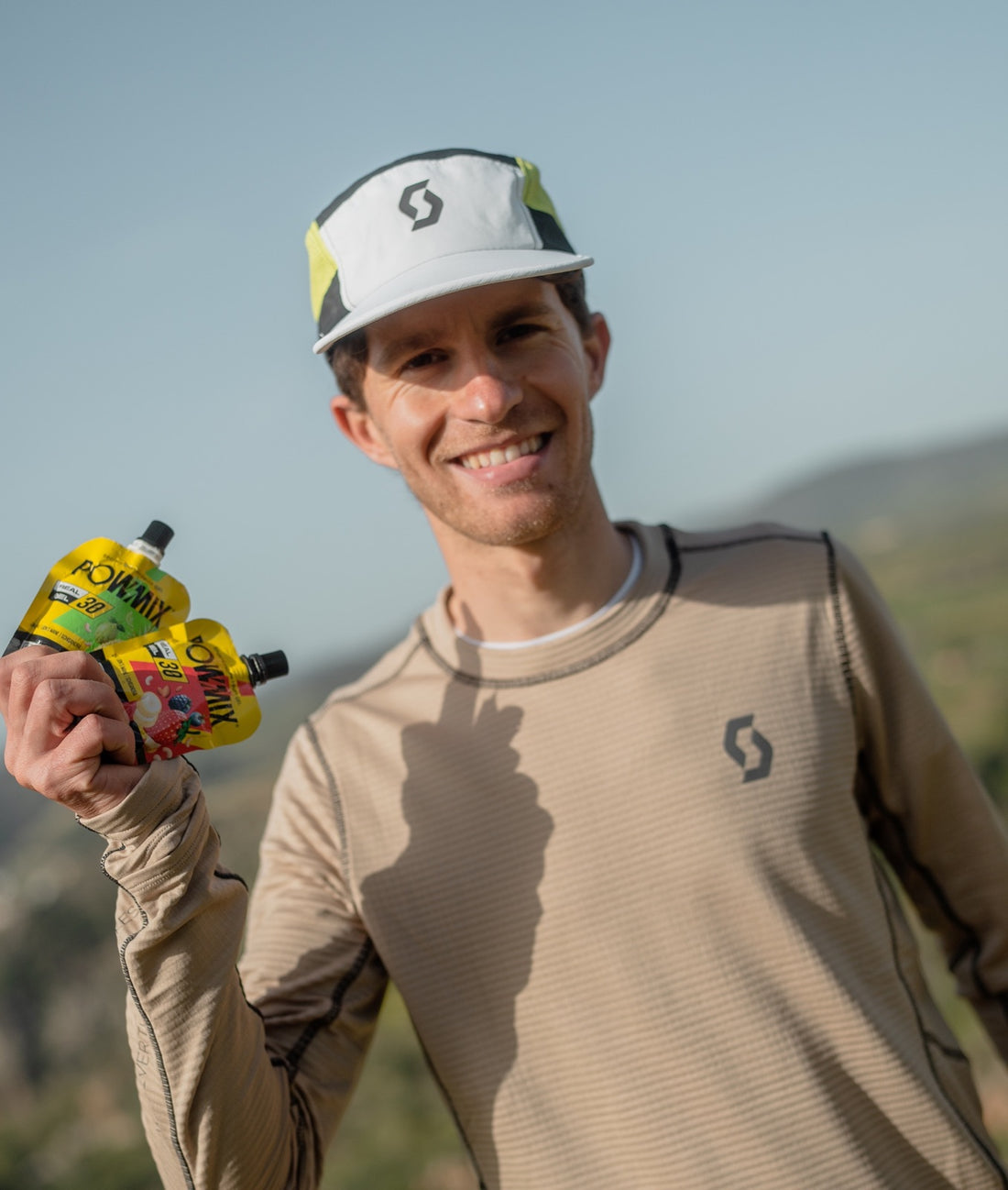 Corredor de trail sonriendo con dos geles POWMIX en la mano