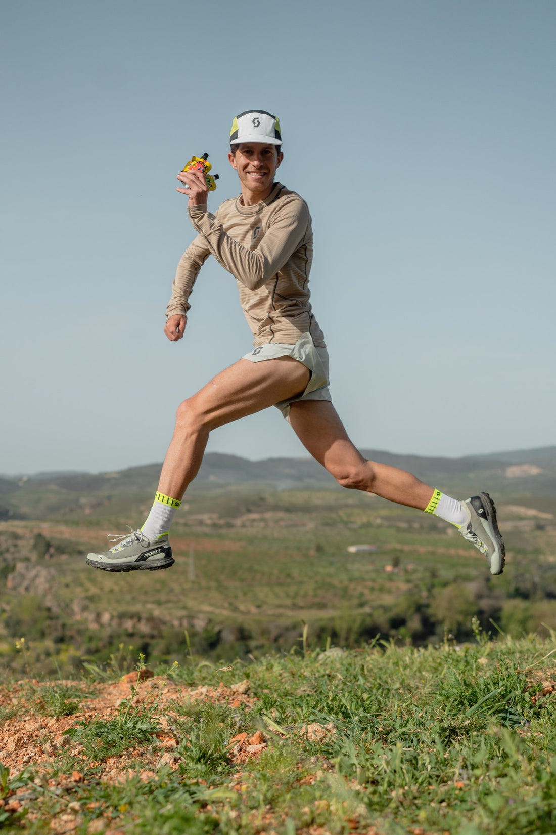 Corredor de trail saltando en la montaña con un gel POWMIX en la mano